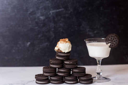 Cookies and Cream protein ball sitting on a stack of Oreo cookies with a glass of milk on a dark background