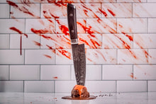 Load image into Gallery viewer, Decorative knife stabbing Chocolate protein truffle coated in rich dark chocolate. With a blood-stained handle on a tiled wall background