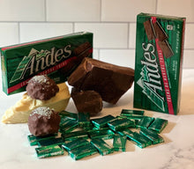 Load image into Gallery viewer, Andes mint chocolate bars and packaging on a marble surface with a white tiled wall background. Sassy Mint protein balls sitting on chunks of chocolate and Andes candy