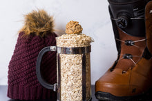 Load image into Gallery viewer, Oatmeal Rasin protein energy bite glamor shot. French press filled with oatmeal next to a knit hat and boots on a white background