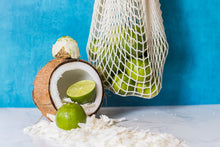Load image into Gallery viewer, Key lime pie protein ball on a coconut with limes
