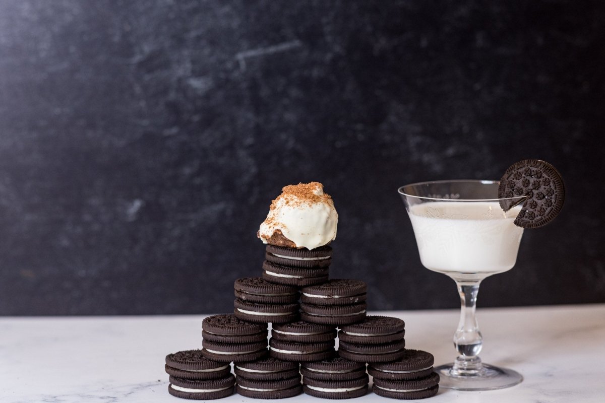 Cookies and Cream protein ball sitting on a stack of Oreo cookies with a glass of milk on a dark background