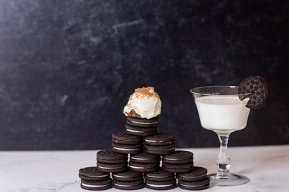 Cookies and Cream protein ball sitting on a stack of Oreo cookies with a glass of milk on a dark background