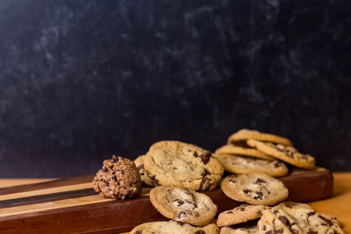 Doughhzer Energy Bites looking dangerously addictive beside a pile of chocolate chip cookies on wooden board, the bad boy your hustle deserves