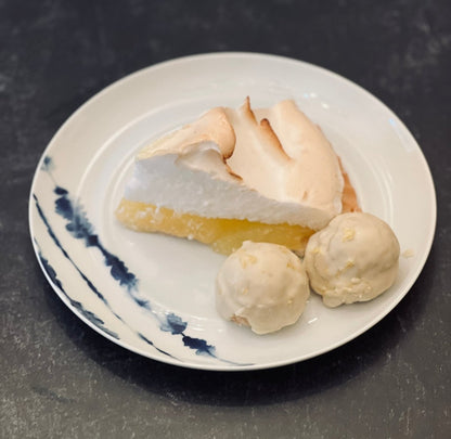 Sassy balls lemon meringue protein ball on a plate next to a slice of lemon meringue pie