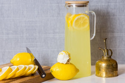 Lemon meringue pie protein ball on top of a lemon in front of a pitcher of lemonade